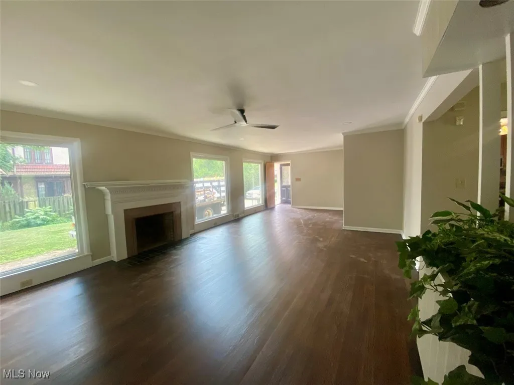 Unfurnished living room with dark wood finished floors, ceiling fan, a fireplace, and ornamental molding