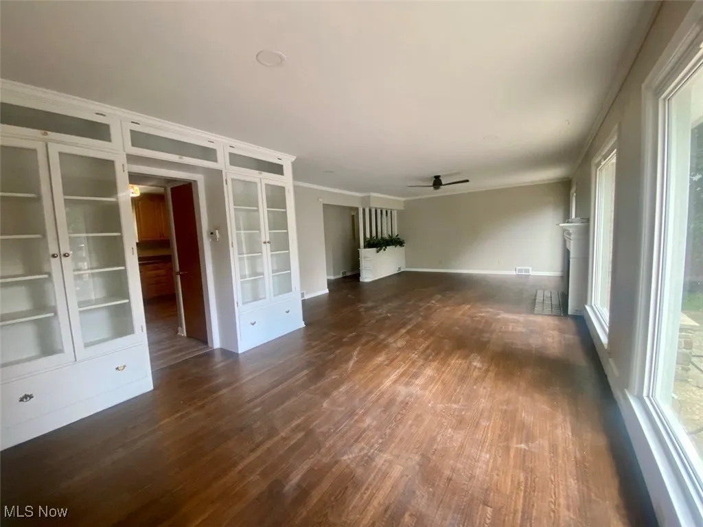 Unfurnished living room featuring french doors, crown molding, dark wood-type flooring, and a ceiling fan