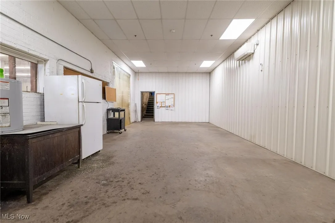 Below grade area with freestanding refrigerator, a wall mounted AC, and a paneled ceiling