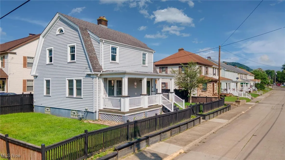 View of front of property featuring a porch, a fenced backyard, a gambrel roof, a chimney, and a shingled roof