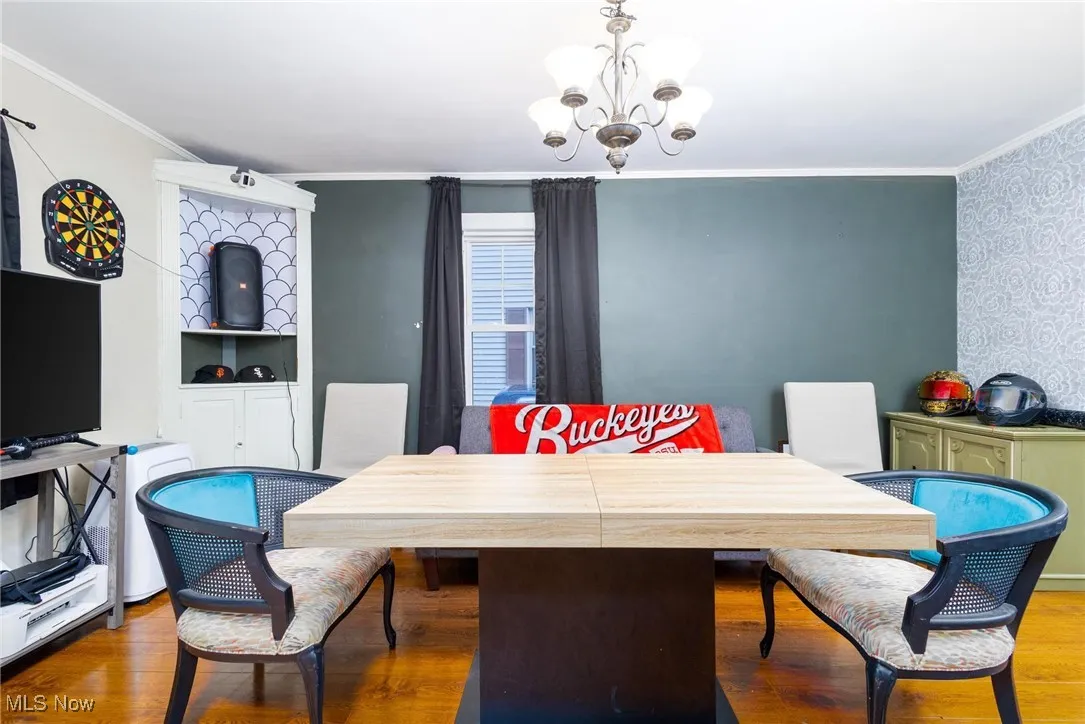 Dining area with a chandelier, crown molding, wood finished floors, and wallpapered walls