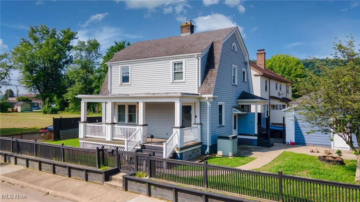 View of front facade with covered porch, a chimney, a fenced front yard, and roof with shingles