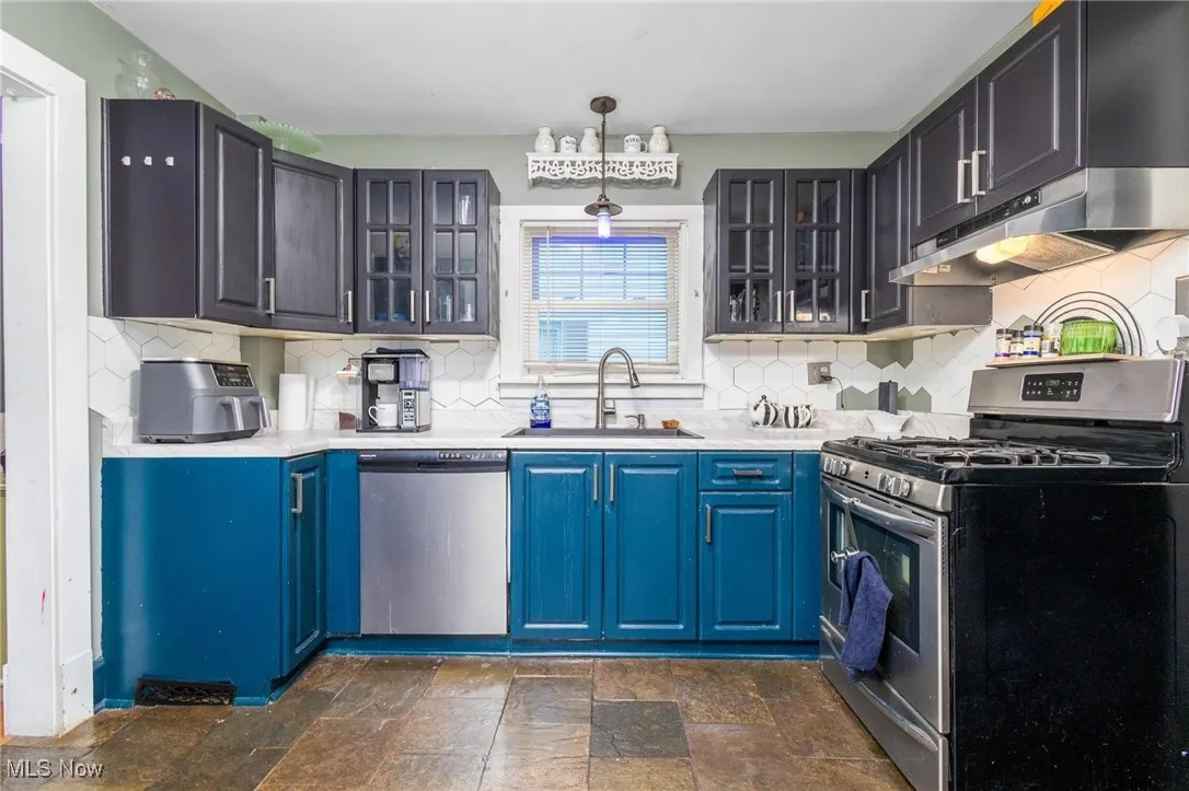 Kitchen featuring appliances with stainless steel finishes, under cabinet range hood, blue cabinetry, and glass insert cabinets