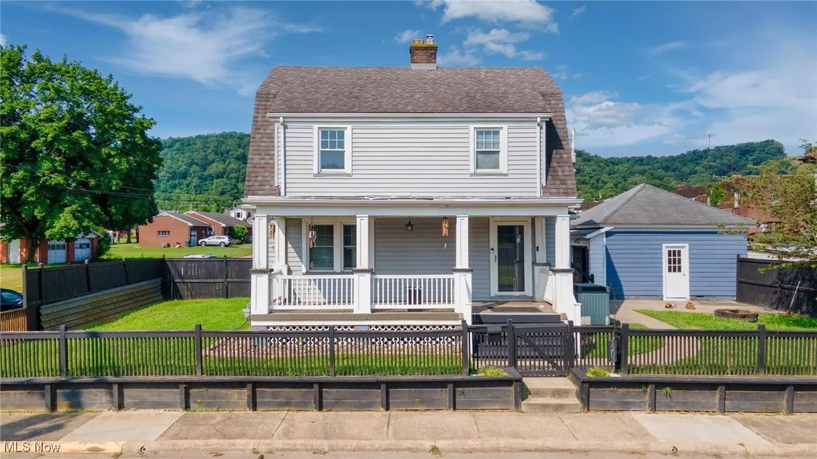 View of front of home featuring a porch, a chimney, a fenced front yard, and roof with shingles
