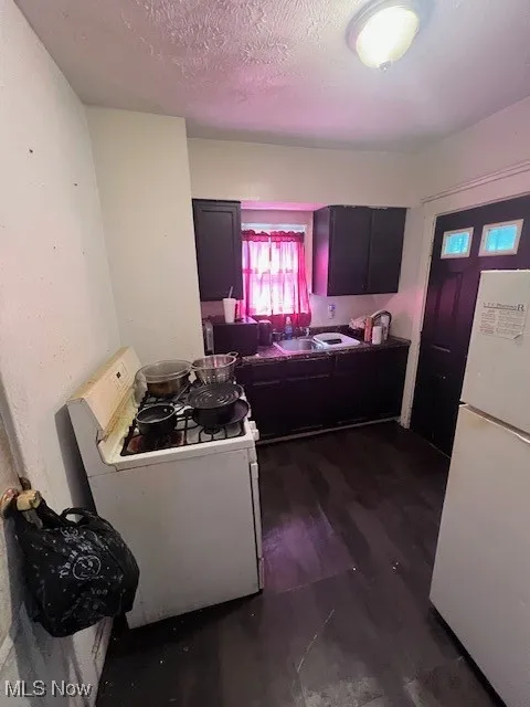 Kitchen featuring refrigerator, stove, dark wood-style floors, and a textured ceiling