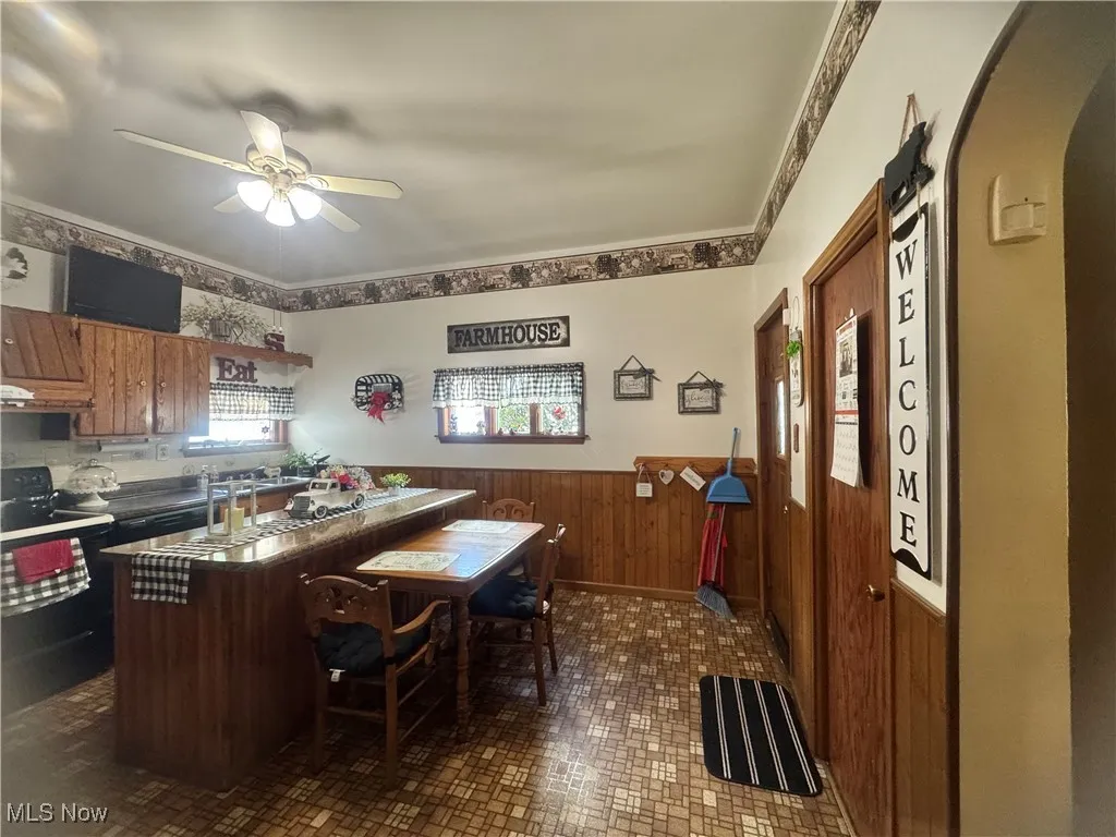 Kitchen with arched walkways, a wainscoted wall, ceiling fan, brown cabinetry, and wood walls