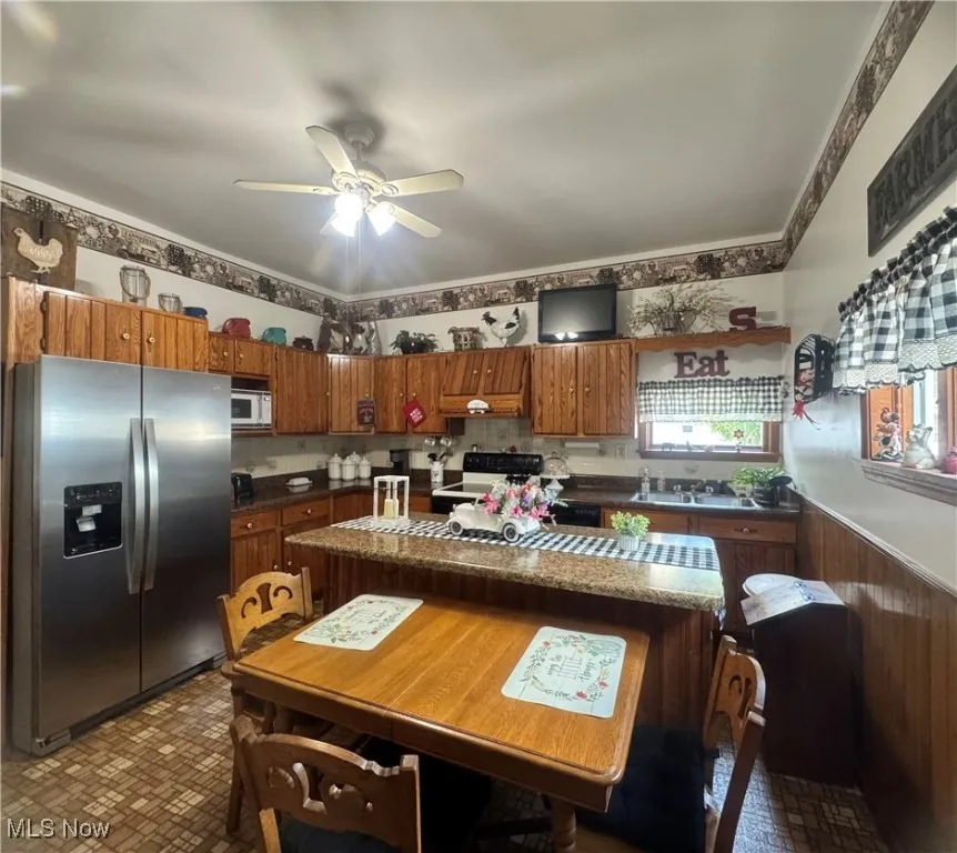 Kitchen with white appliances, brick patterned floors, brown cabinets, and ceiling fan