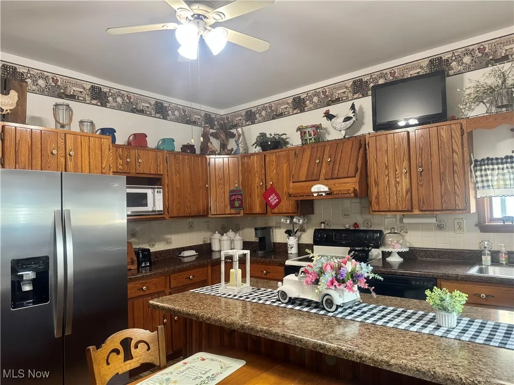 Kitchen featuring stainless steel fridge, electric stove, white microwave, brown cabinets, and a ceiling fan