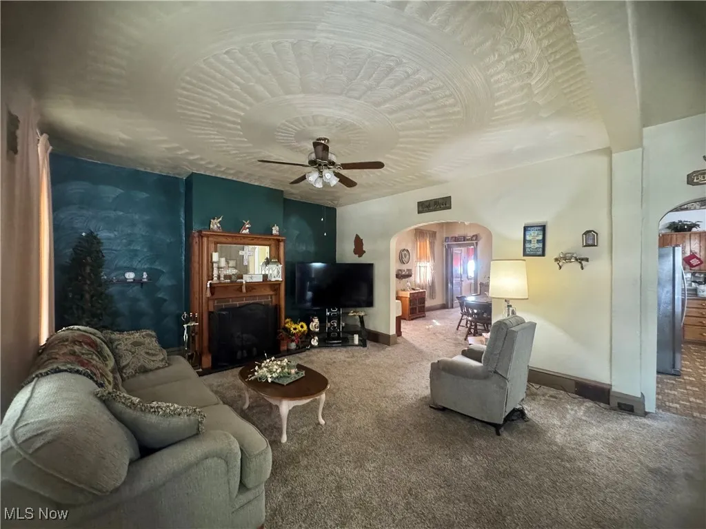Carpeted living area with arched walkways, ceiling fan, and a brick fireplace