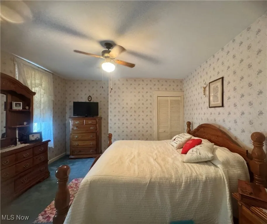 Carpeted bedroom featuring wallpapered walls, a ceiling fan, and a closet