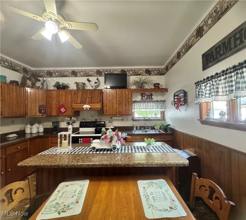 Kitchen featuring electric range oven, brown cabinets, ceiling fan, a wainscoted wall, and a center island