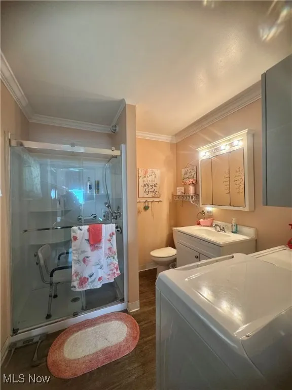 Full bath featuring ornamental molding, wood finished floors, washing machine and clothes dryer, a shower stall, and vanity