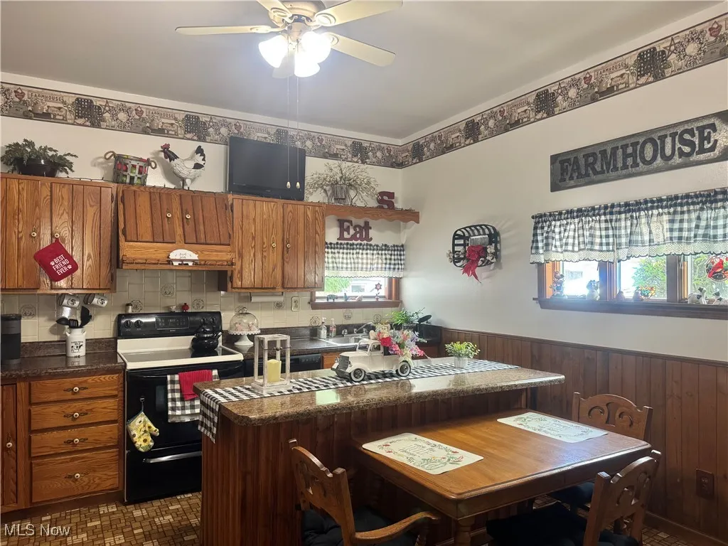 Kitchen with range with electric cooktop, ceiling fan, brown cabinets, healthy amount of natural light, and wainscoting