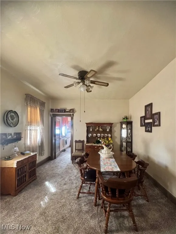 Carpeted dining area with ceiling fan and baseboards