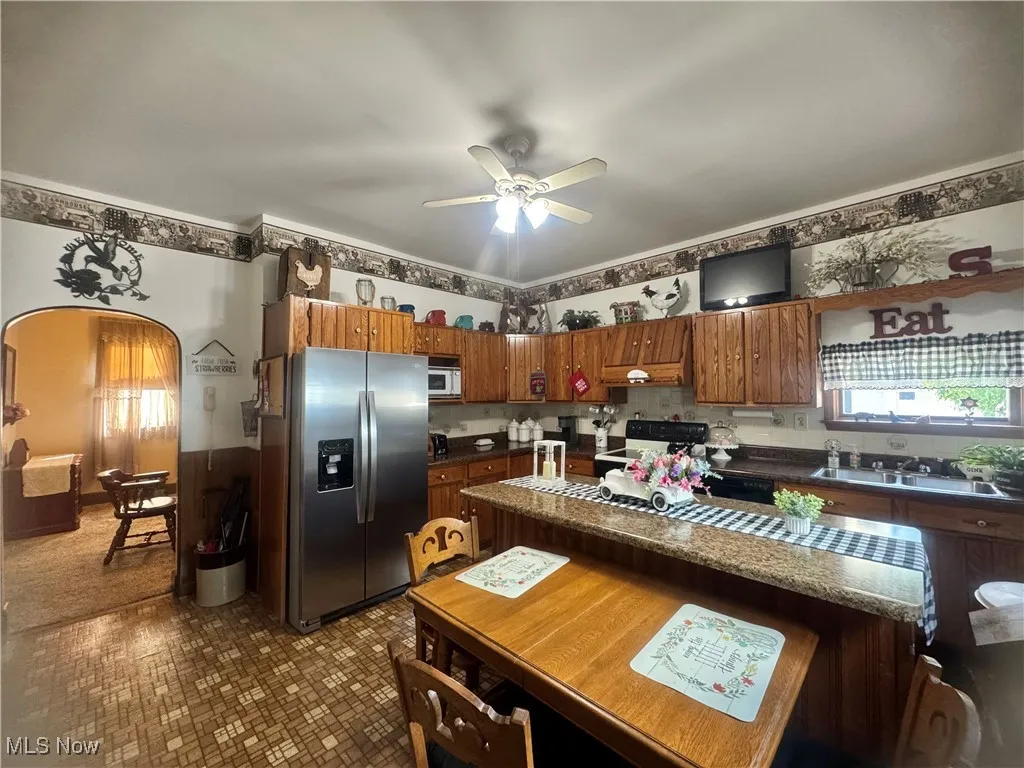 Kitchen with stainless steel fridge, dark countertops, black range with electric stovetop, white microwave, and ceiling fan