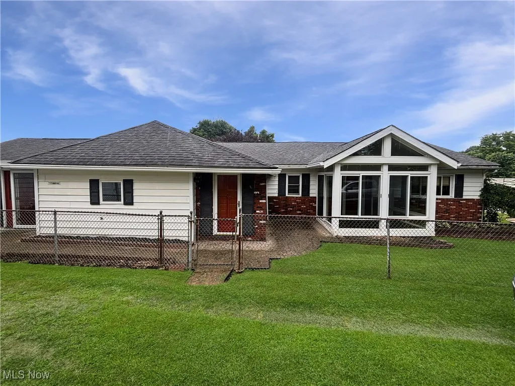 Rear view of house featuring brick siding, roof with shingles, and a sunroom