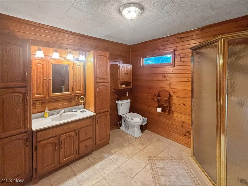 Bathroom with a stall shower, vanity, and wood walls