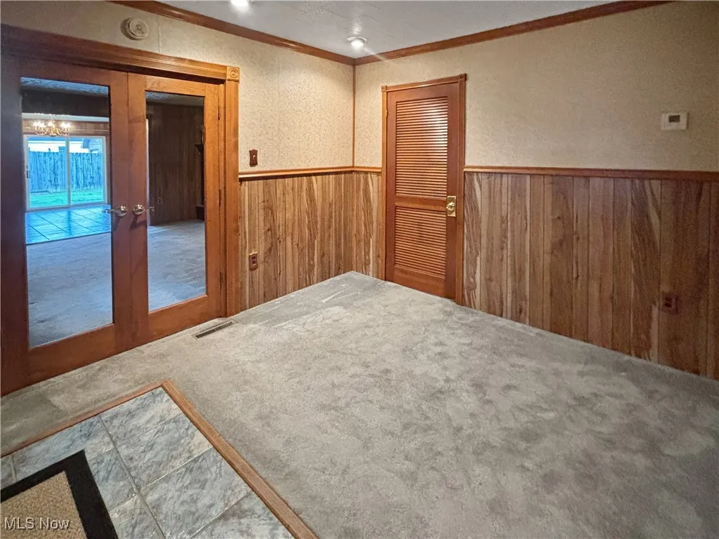 Empty room with crown molding, wooden walls, wainscoting, and french doors
