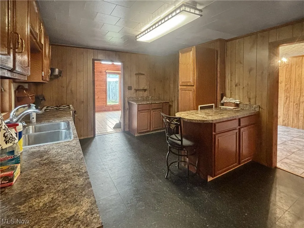 Kitchen featuring wooden walls, brown cabinets, and dark flooring