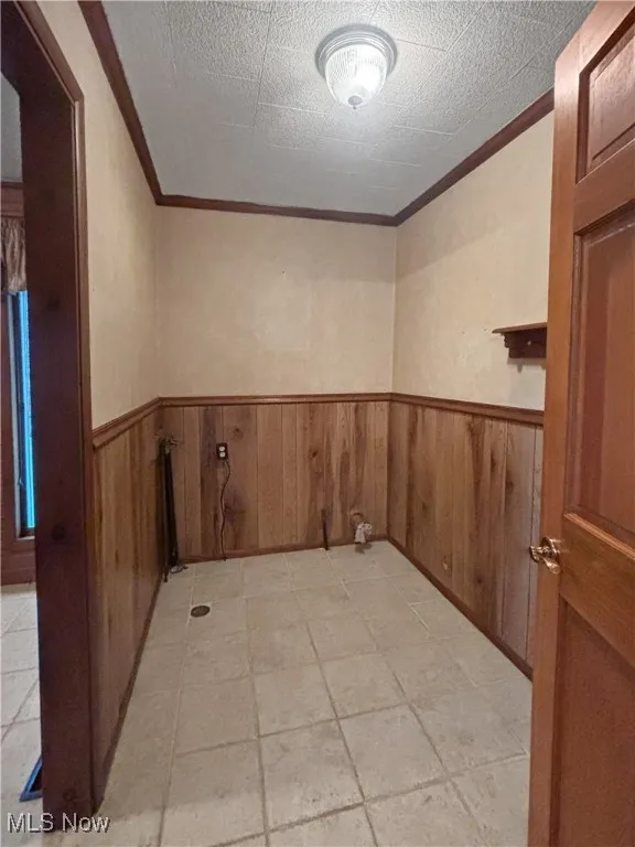 Empty room featuring ornamental molding, wainscoting, and wooden walls