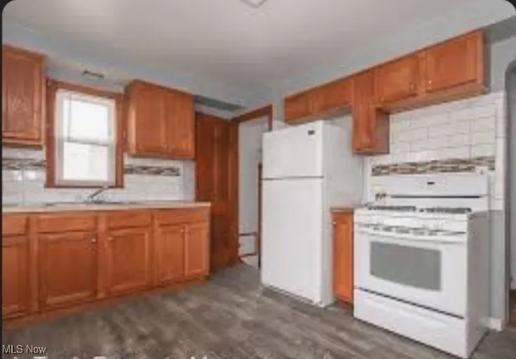 Kitchen featuring white appliances, tasteful backsplash, brown cabinets, light countertops, and dark wood finished floors