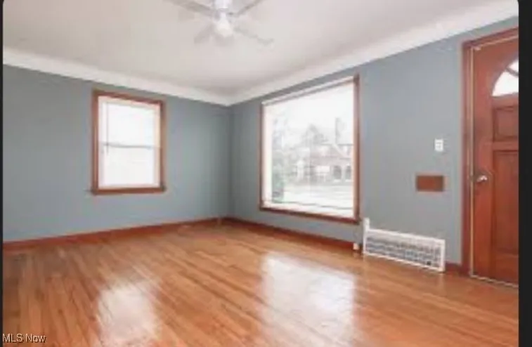 Empty room with wood finished floors, ceiling fan, and ornamental molding