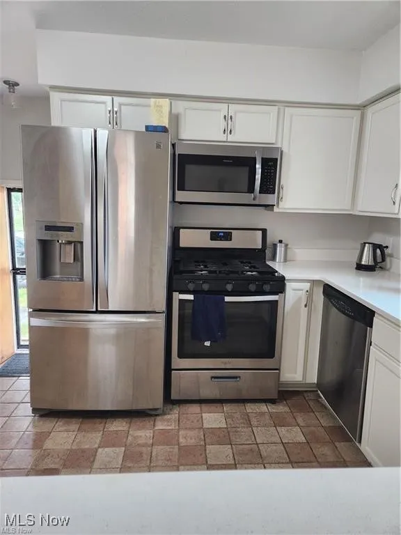 Kitchen featuring appliances with stainless steel finishes, white cabinetry, and light countertops