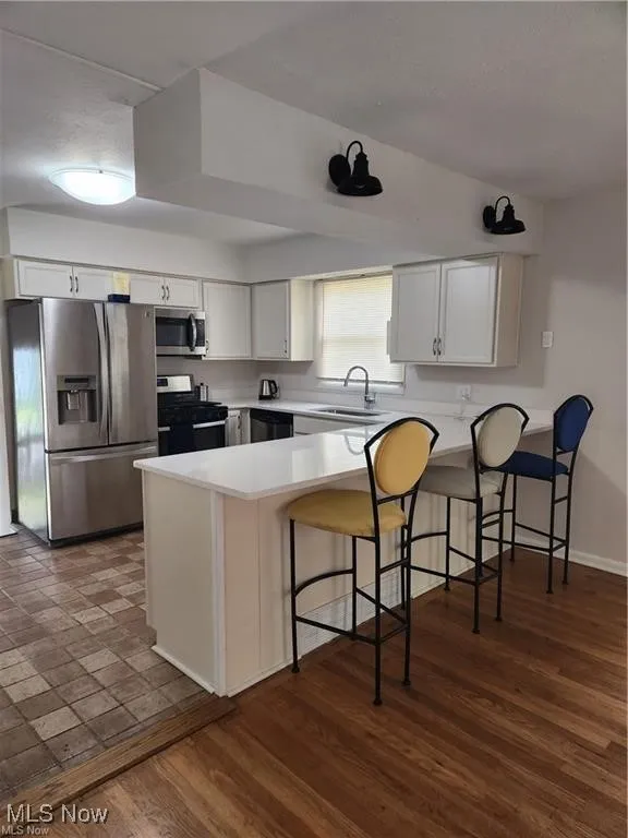 Kitchen featuring appliances with stainless steel finishes, a peninsula, light countertops, and a kitchen breakfast bar