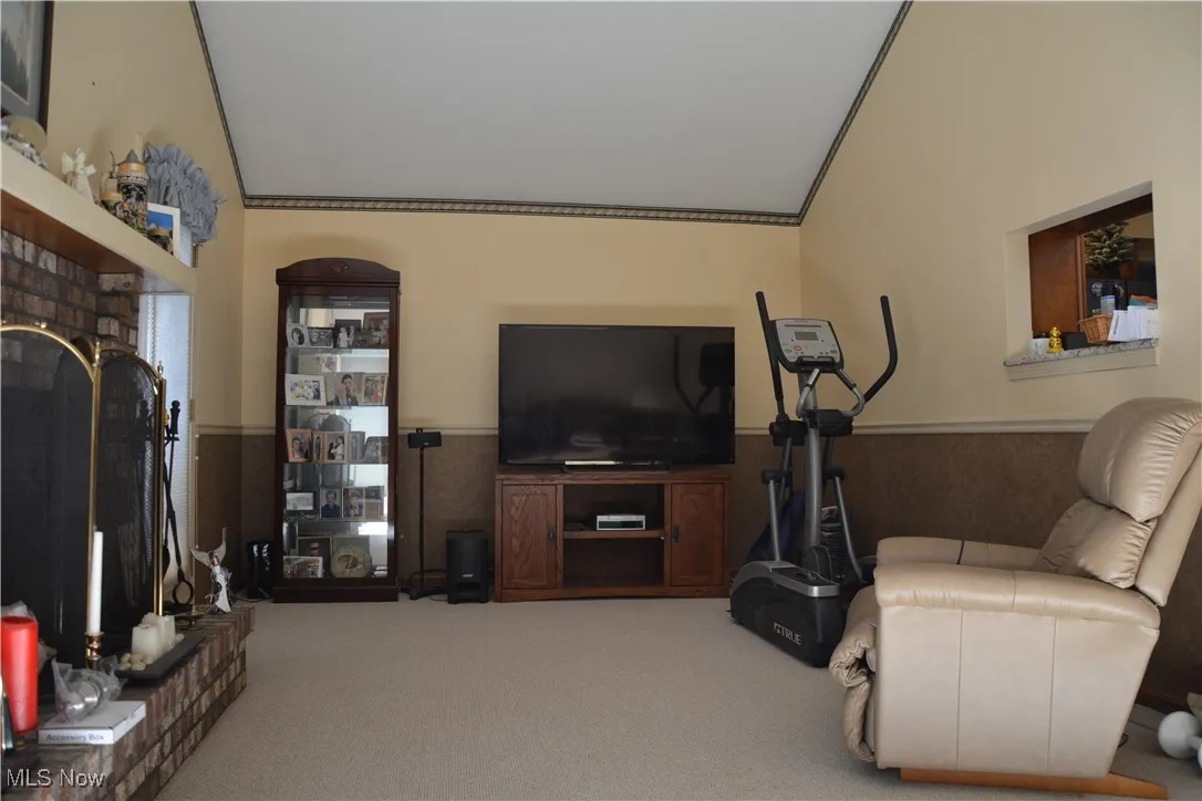 Carpeted family room with a fireplace, a wainscoted wall, and vaulted ceiling
