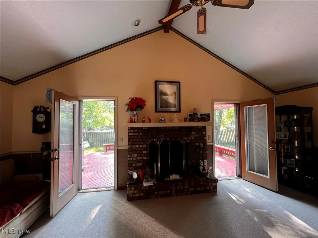 Carpeted living area with healthy amount of natural light, ceiling fan, a brick fireplace, and crown molding