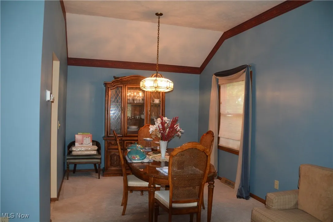 Dining space featuring a chandelier, light colored carpet, crown molding, and lofted ceiling