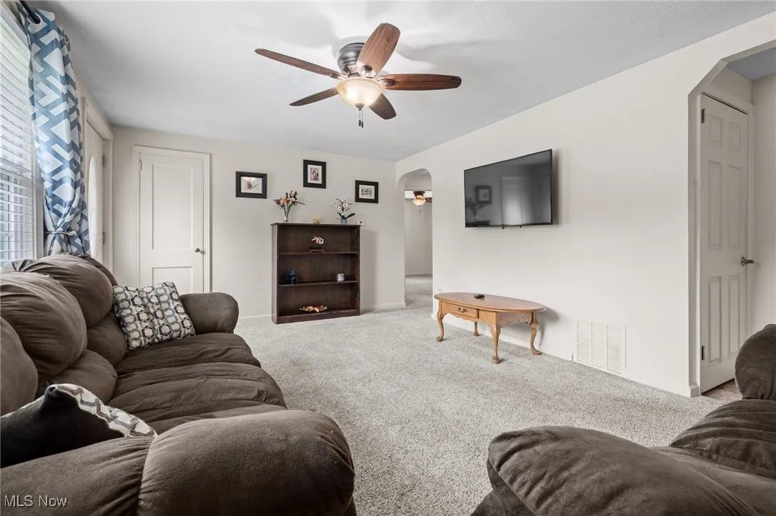 Living room featuring arched walkways, ceiling fan/light, picture window, coat closet and carpeted floors