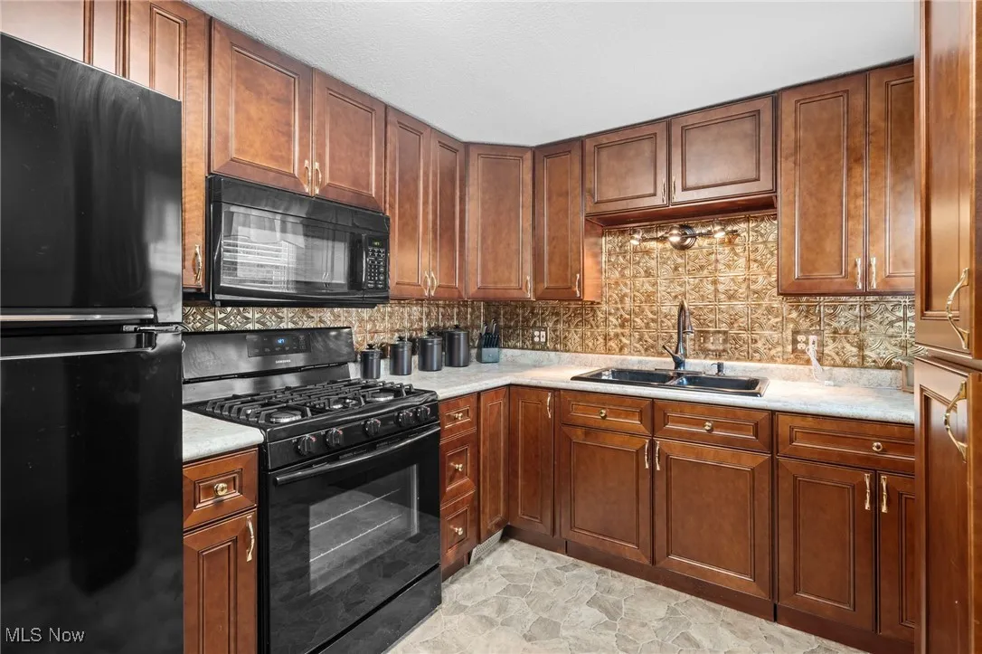 Kitchen featuring black appliances, light countertops, tasteful backsplash, and brown raised panel cabinets