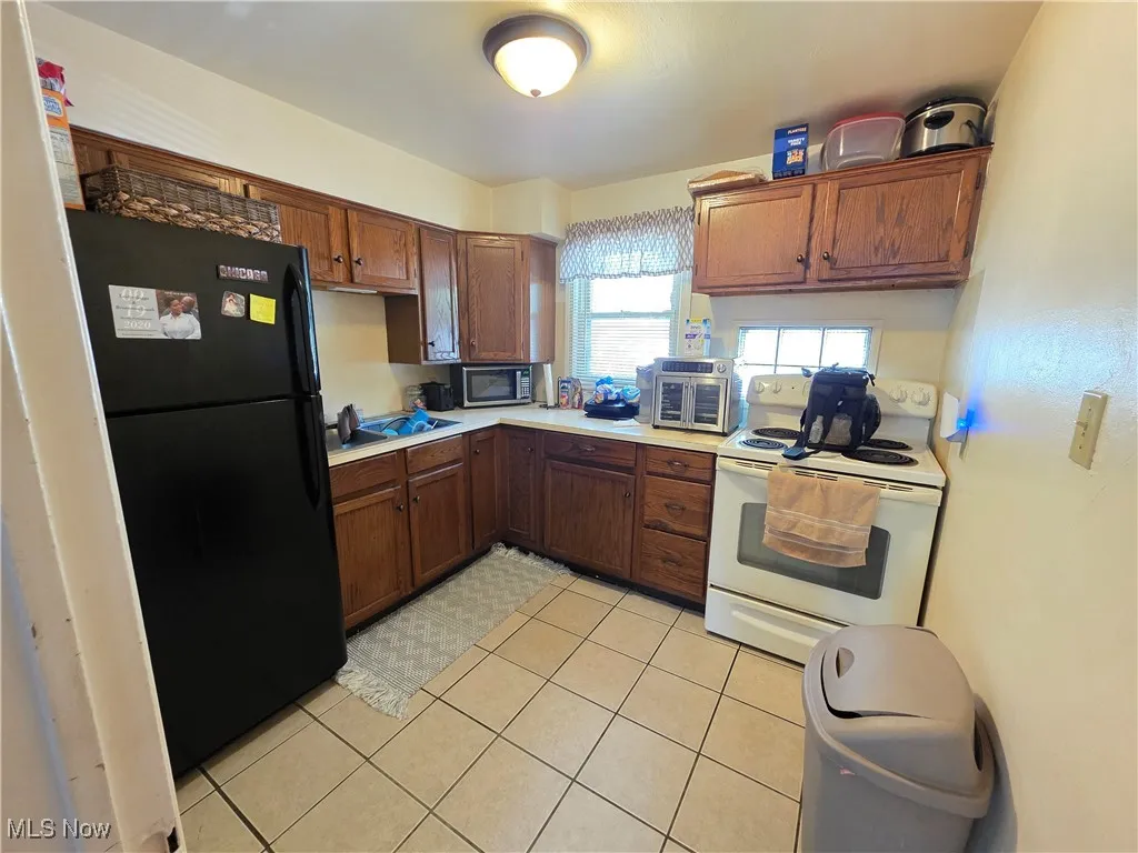 Kitchen featuring freestanding refrigerator, white electric range, stainless steel microwave, light countertops, and brown cabinets