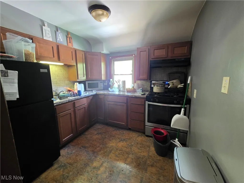 Kitchen featuring freestanding refrigerator, stainless steel gas range, white microwave, under cabinet range hood, and tasteful backsplash