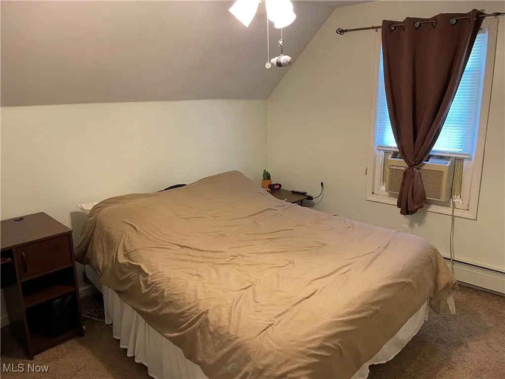 Carpeted bedroom featuring vaulted ceiling, baseboard heating, and cooling unit