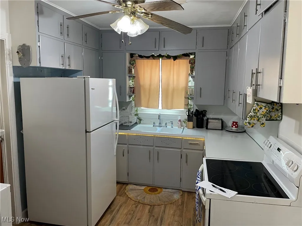 Kitchen featuring white appliances, gray cabinets, wood finished floors, light countertops, and ceiling fan