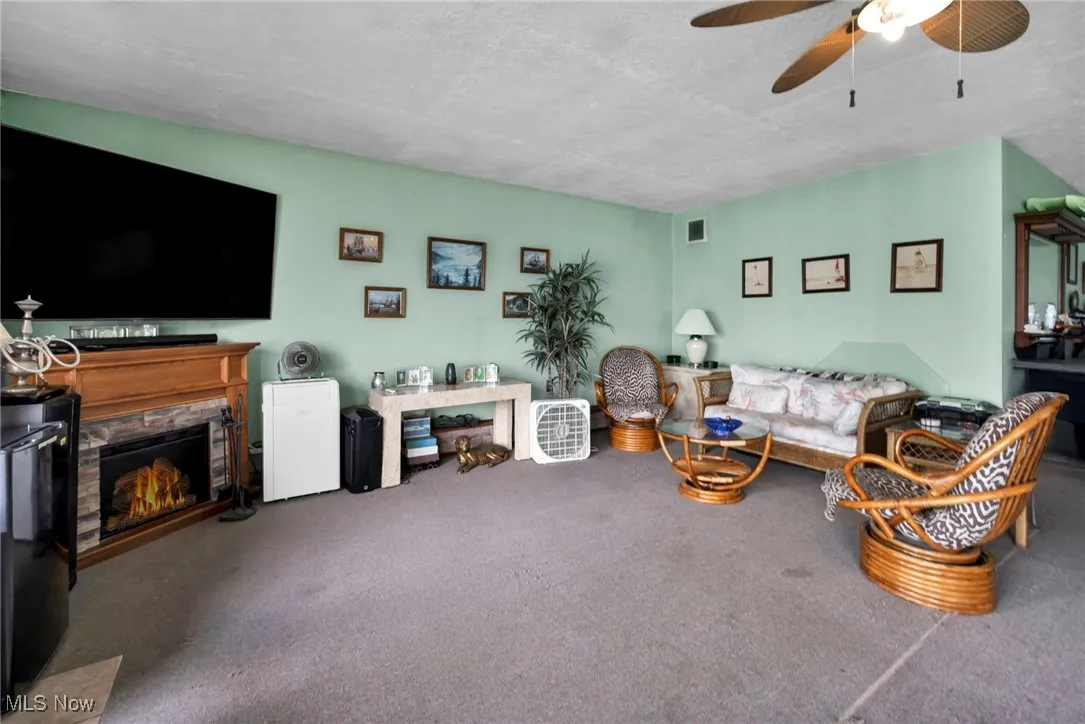 Carpeted living room with ceiling fan and a warm lit fireplace