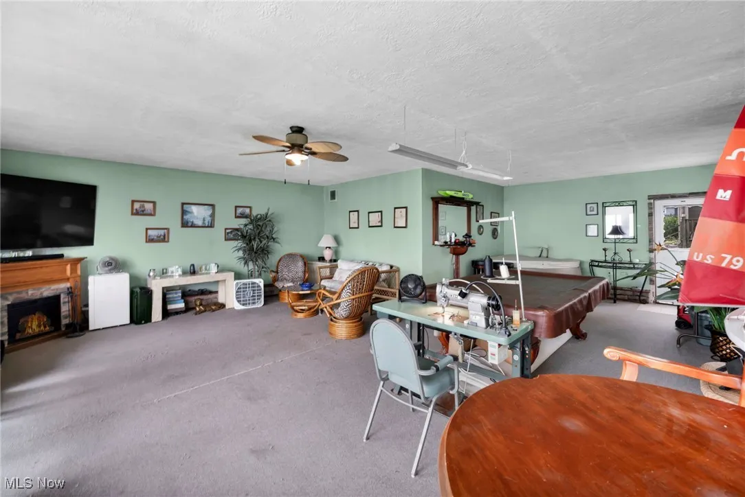Living area featuring ceiling fan, carpet floors, billiards table, a textured ceiling, and a stone fireplace