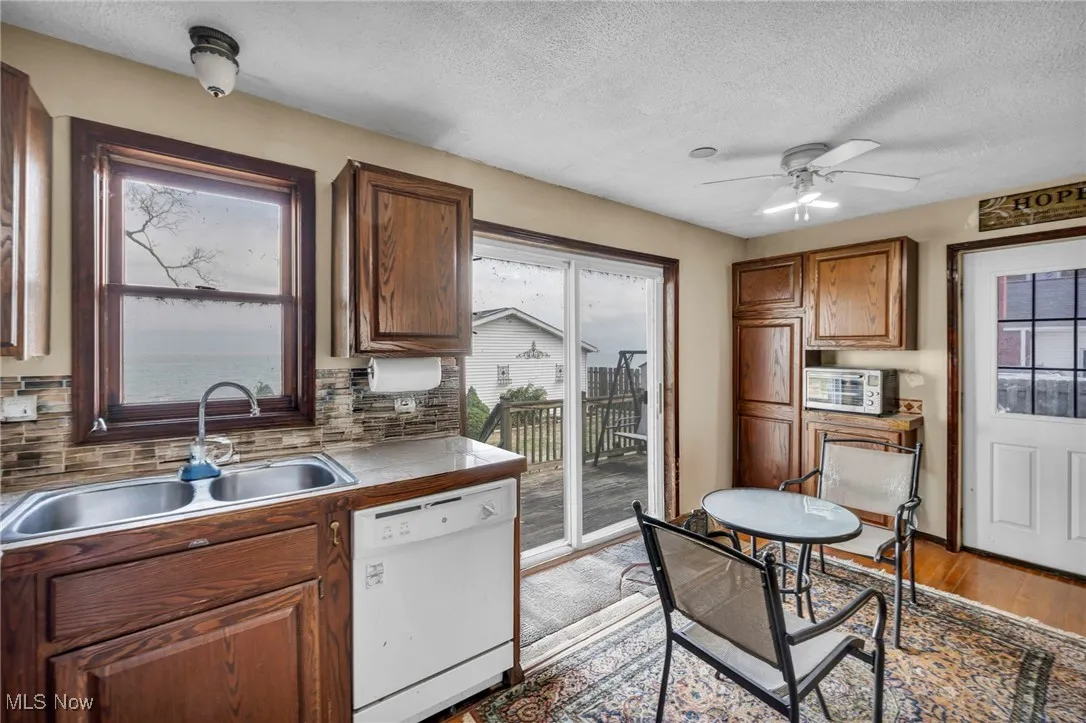 Kitchen with white dishwasher, backsplash, ceiling fan, a textured ceiling, and light wood-type flooring