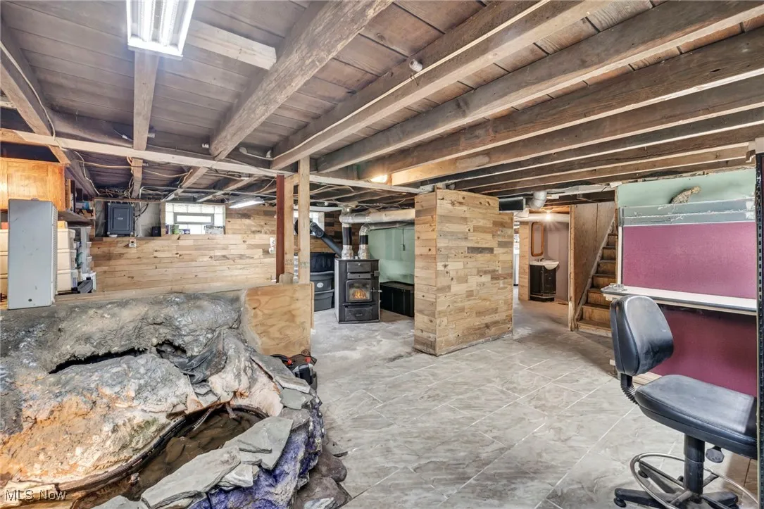 Basement featuring wood walls, a wood stove, stairs, and electric panel