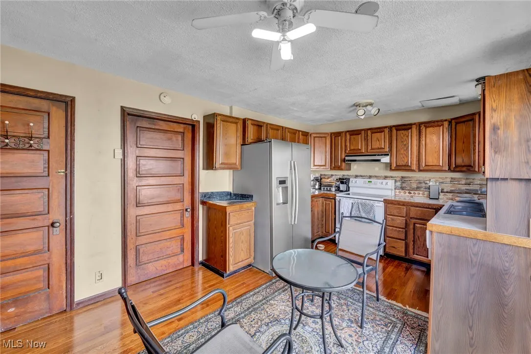 Kitchen featuring white electric range, stainless steel fridge with ice dispenser, under cabinet range hood, brown cabinetry, and a textured ceiling