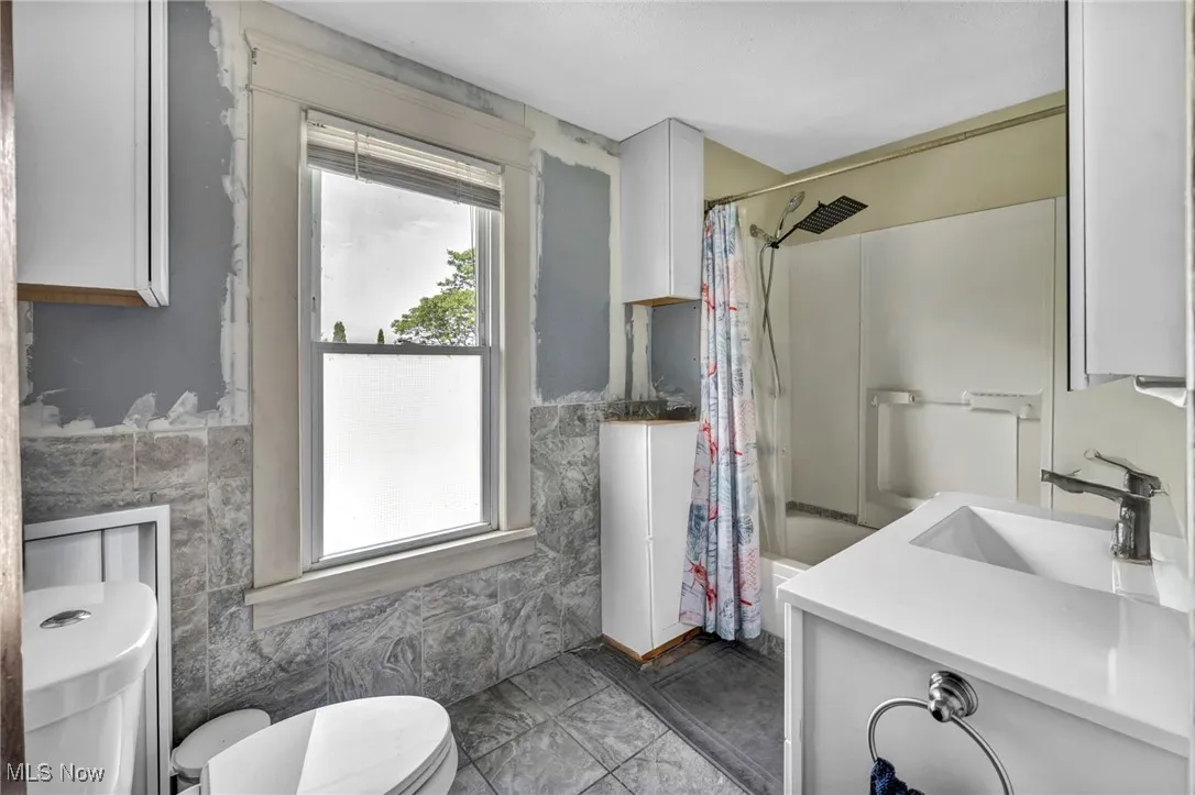 Bathroom featuring tile walls, vanity, shower / tub combo, and wainscoting