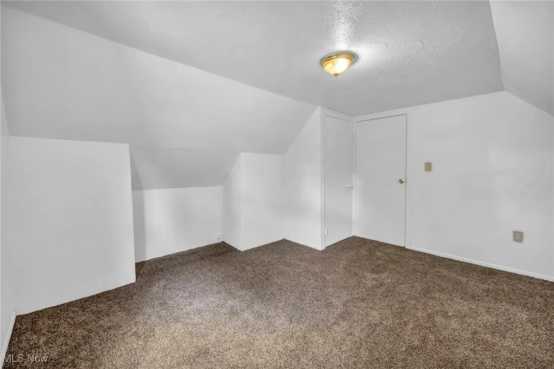 Additional living space with vaulted ceiling, carpet floors, and a textured ceiling