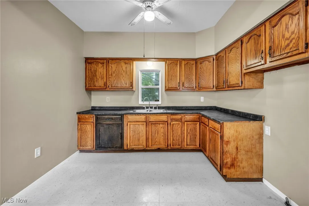 Kitchen with brown cabinetry, ceiling fan, dark countertops, and light flooring