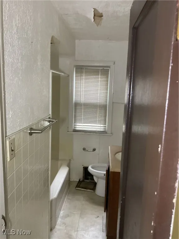Bathroom with vanity, shower / tub combination, tile patterned floors, and tile walls