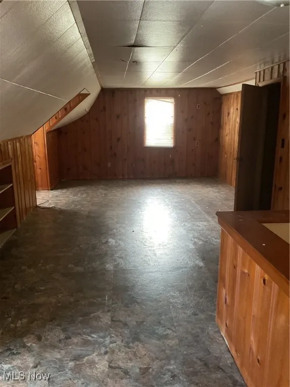 Additional living space featuring dark flooring, wood walls, and vaulted ceiling