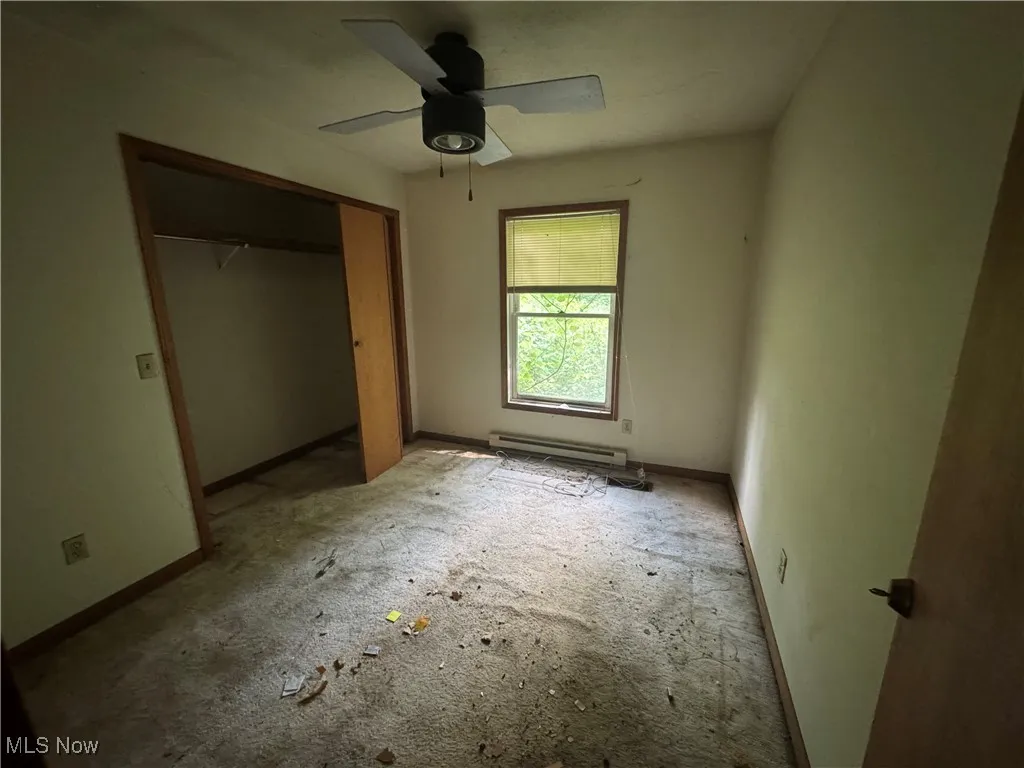 Unfurnished bedroom with a closet, baseboard heating, and a ceiling fan