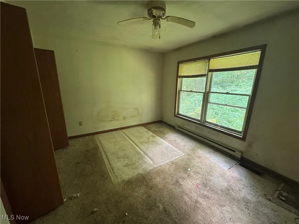 Empty room featuring a baseboard heating unit, carpet floors, and ceiling fan