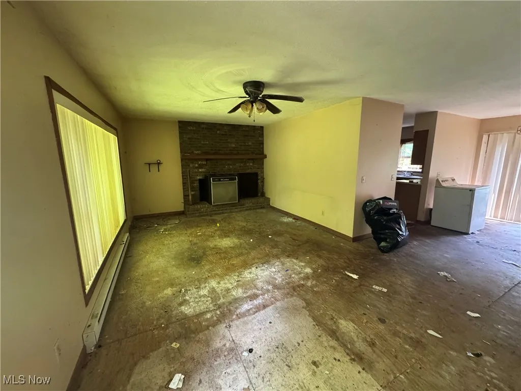 Unfurnished living room with a ceiling fan, baseboard heating, a fireplace, and washer / clothes dryer